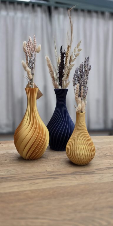 Drie vazen in verschillende kleuren en vormen met gedroogde bloemen.