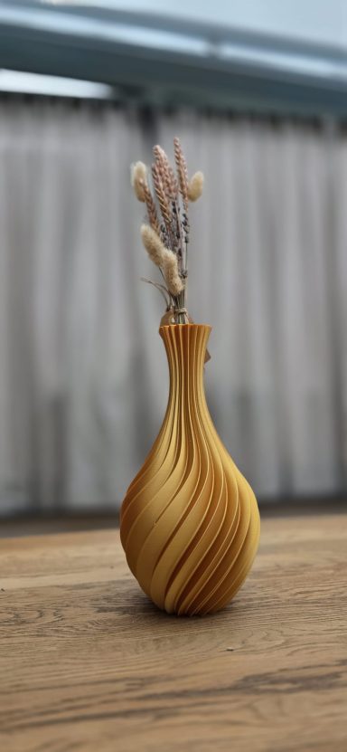 Gele, spiraalvormige vaas met gedroogde bloemen op een houten tafel.