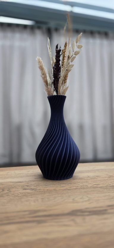 Donkerblauwe vaas met droogbloemen, geplaatst op een houten tafel.