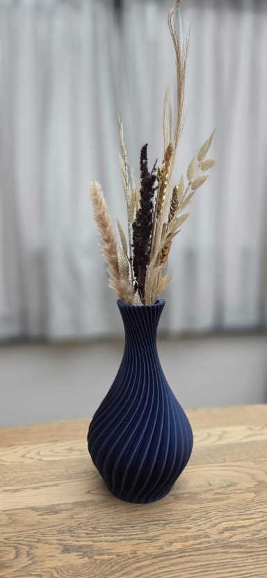 Donkerblauwe vaas met droogbloemen op een houten tafel, achtergrond met gordijnen.